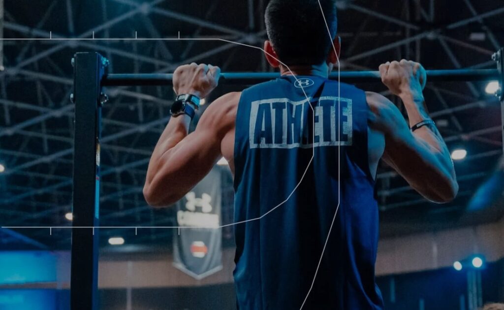 Athlete performing pull-ups in a gym with 'ATHLETE' printed on the back of their shirt.